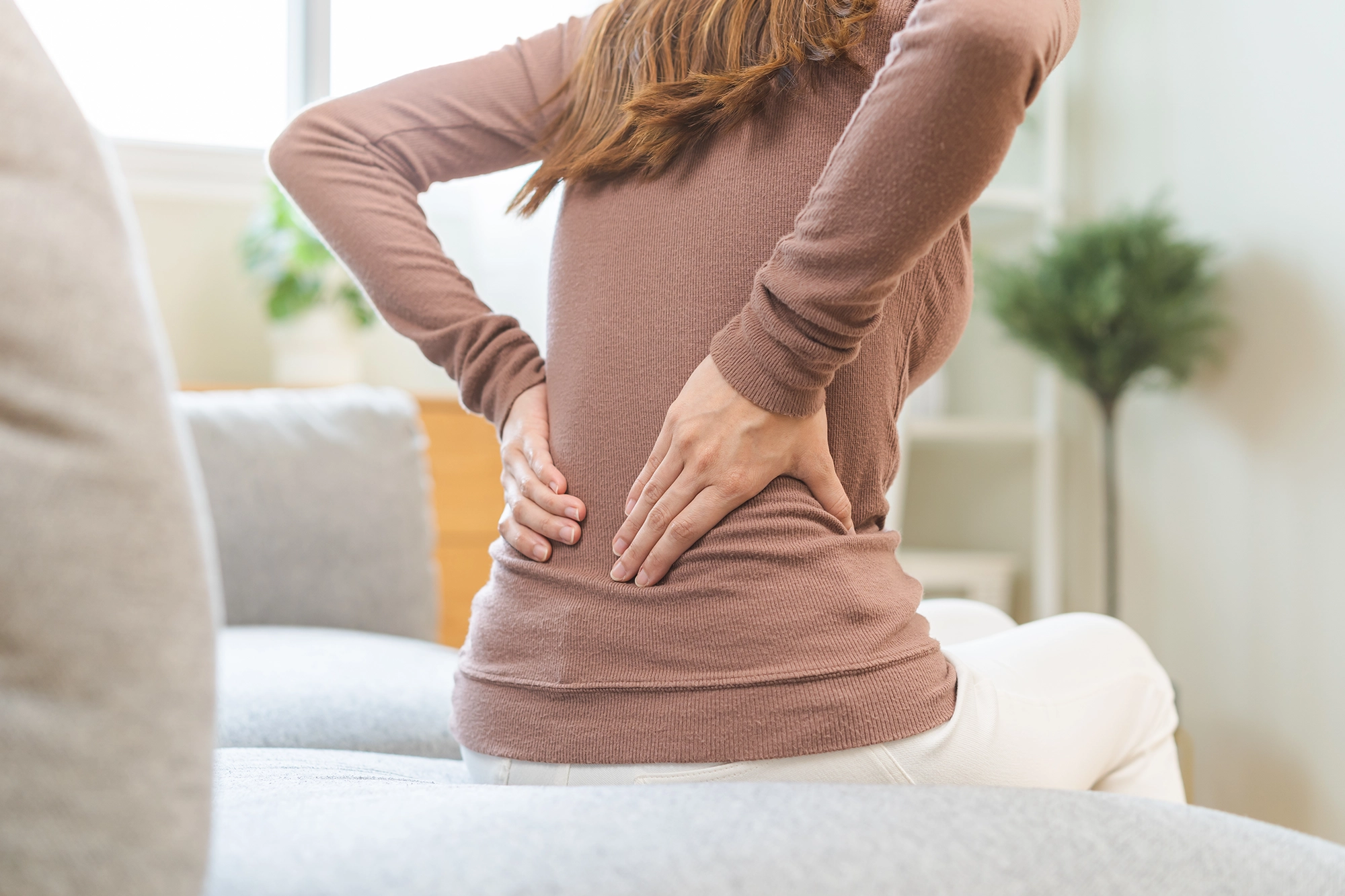 Asian lady clutching her lower pain, illustrating back pain and discomfort.