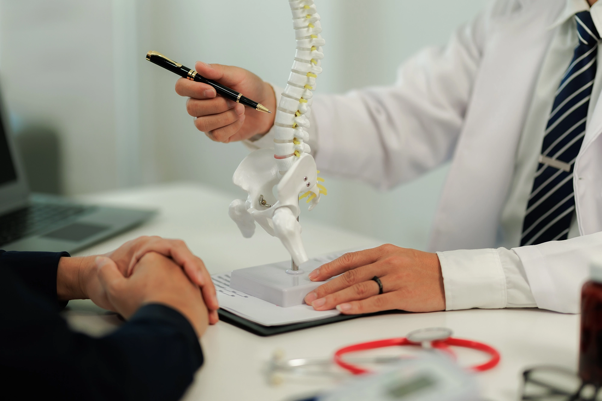 Doctor consulting with a patient who is suffering from back pain, discussing symptoms and potential treatment options in a clinical setting.