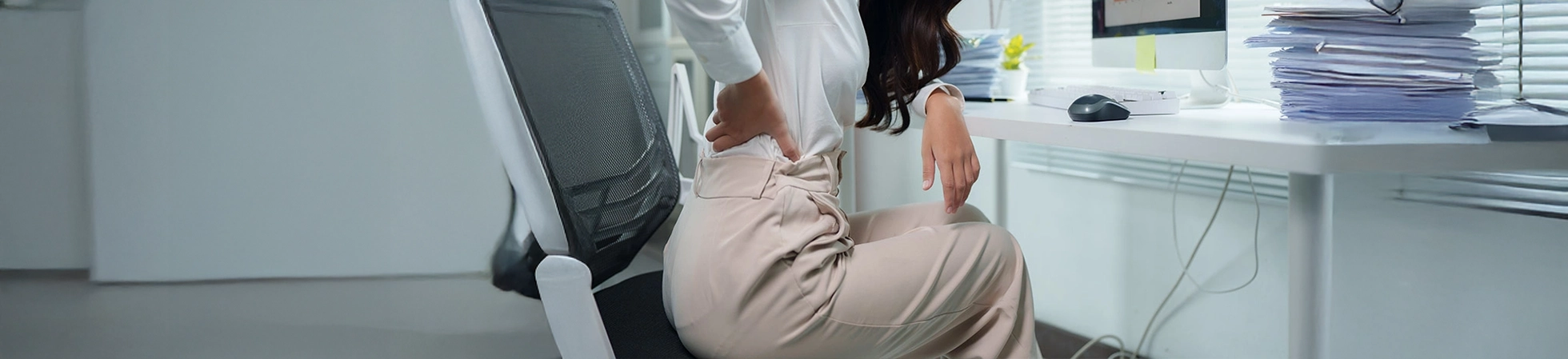 Office worker sitting at a desk and holding their lower back in discomfort, illustrating work‑related back pain.