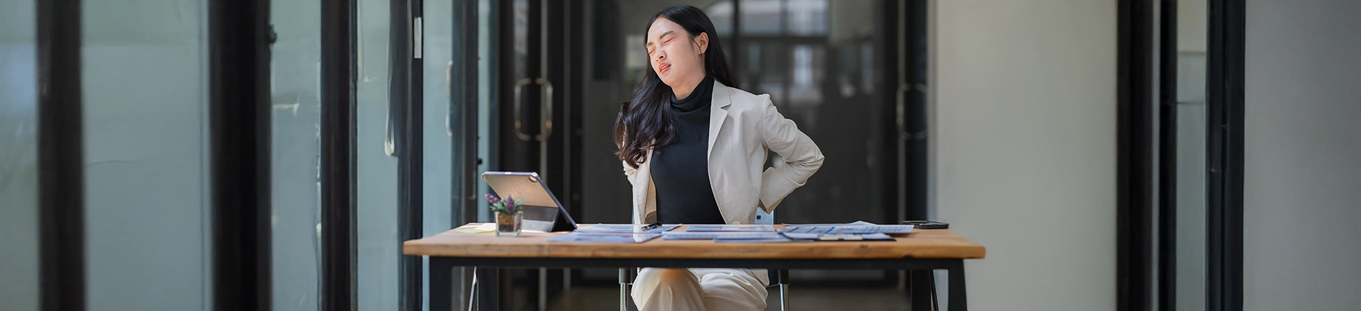 Asian woman grimacing and holding her lower back in pain, illustrating discomfort from lower back strain or injury.