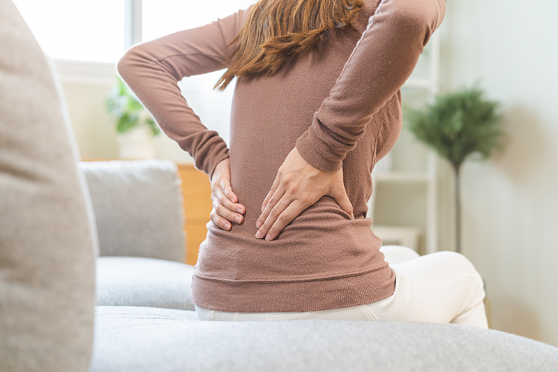 Woman holding her lower back, illustrating back pain that may be linked to knee issues.