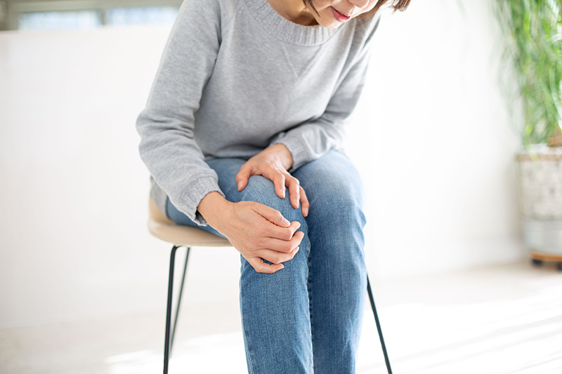 Woman clutching her knee in discomfort, representing knee pain symptoms.