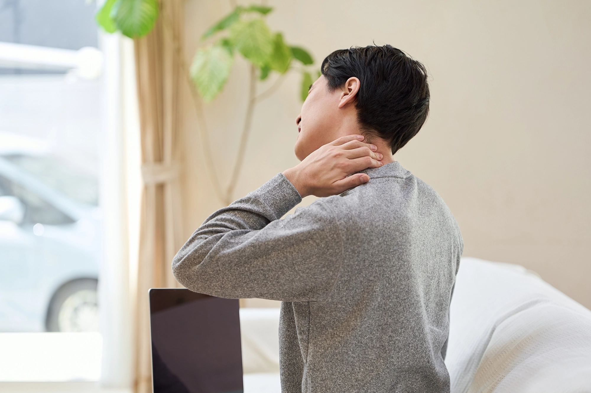 Man sitting and holding his neck, illustrating discomfort or stiffness in the neck area.
