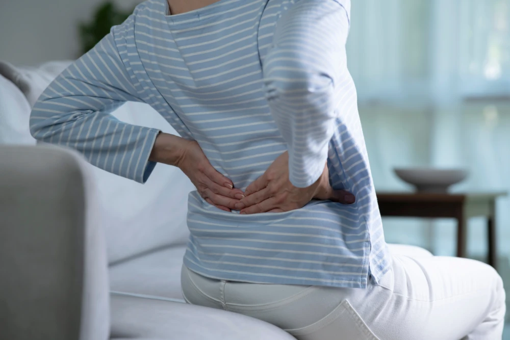 Woman sitting and holding her lower back due to pain