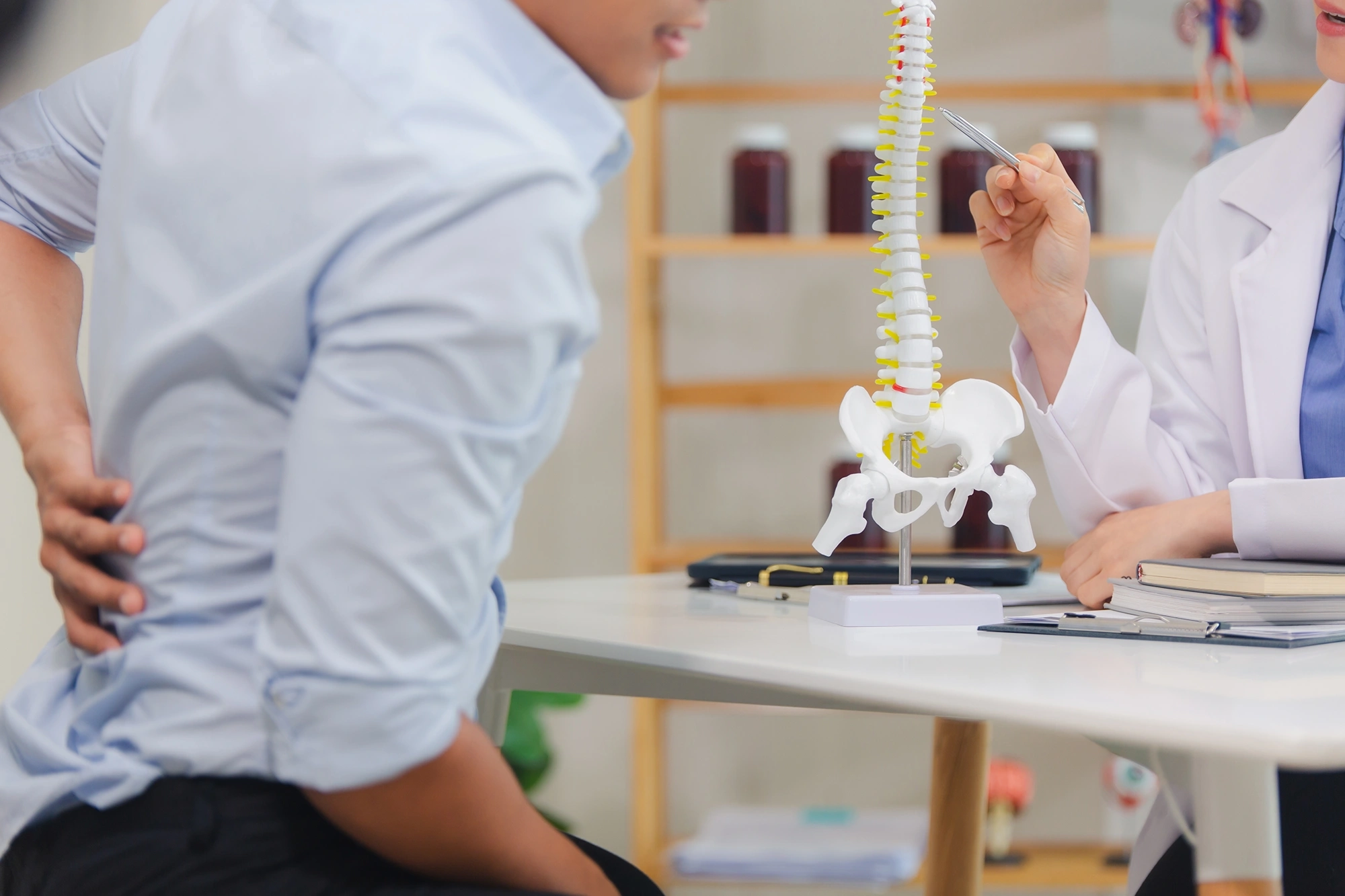 Doctor shows a spinal model to a patient with back pain