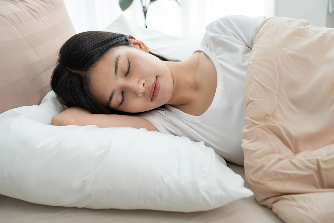 Asian woman sleeping peacefully in bed, illustrating restful sleep.