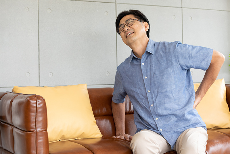 Man at home holding his lower back in discomfort due to sciatica-related pain.