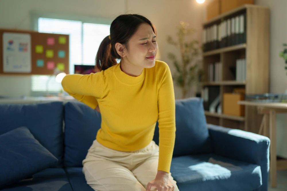 Woman sitting with one hand on her lower back due to back pain.