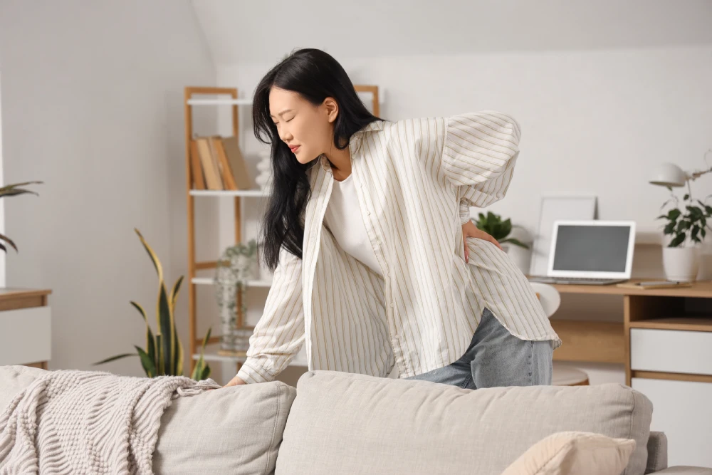 Woman standing and holding her lower back while experiencing sharp back pain.