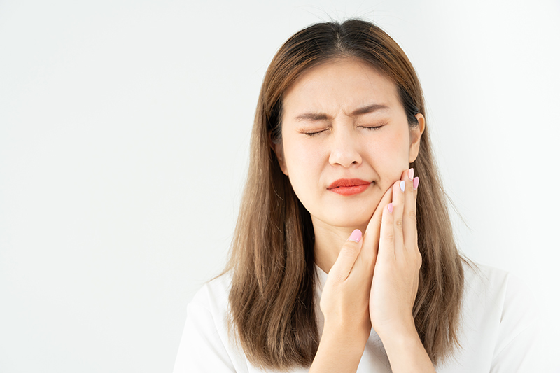 Woman holding her cheek in discomfort due to sudden facial pain.