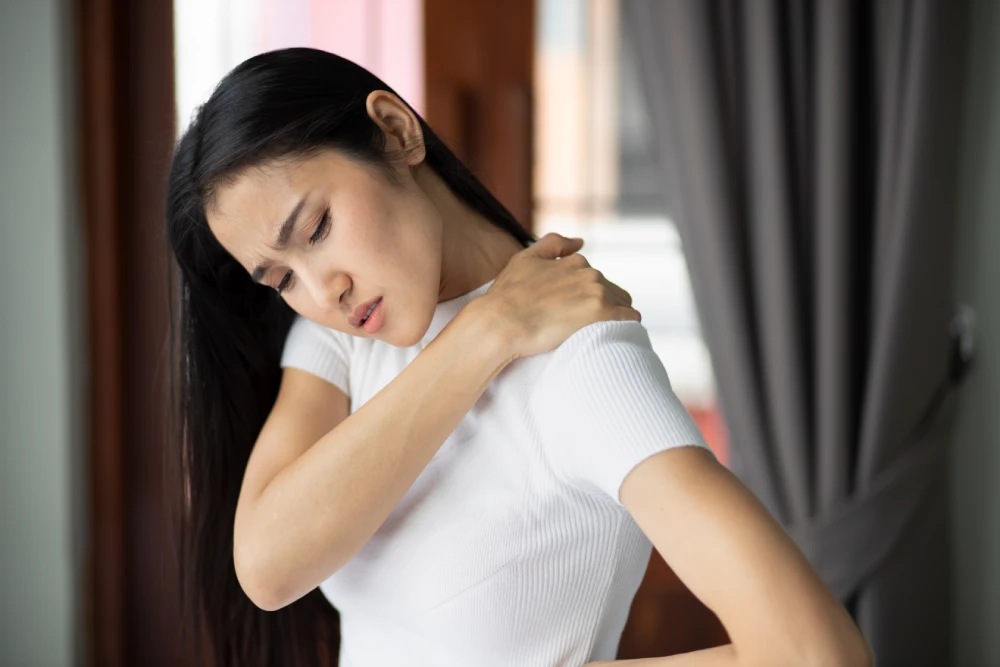 Woman holding her shoulder while experiencing pain and discomfort.