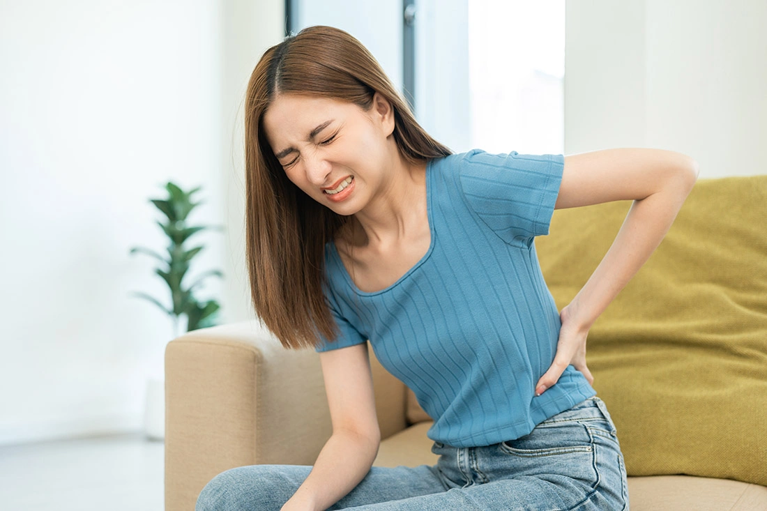 Asian woman touching her lower back with a pained expression, illustrating back pain.