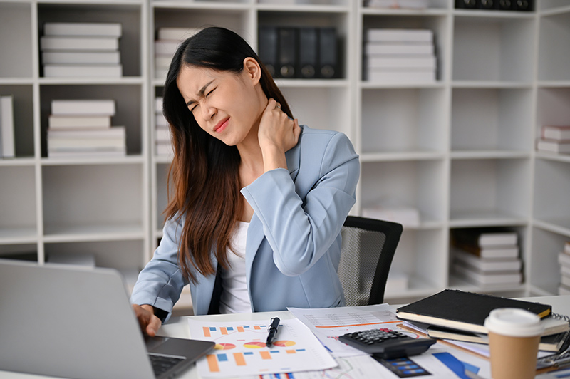 Woman in office attire pressing her neck and shoulder, indicating work-related neck pain.